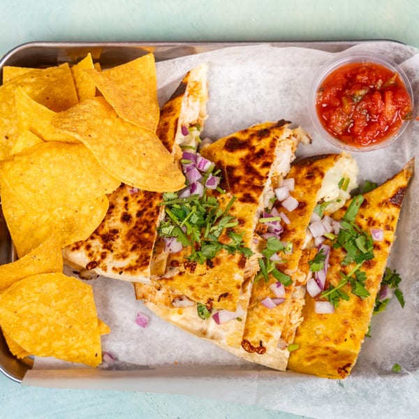 Quesadillas with red onions and cilantro, tortilla chips, and salsa on a metal tray.