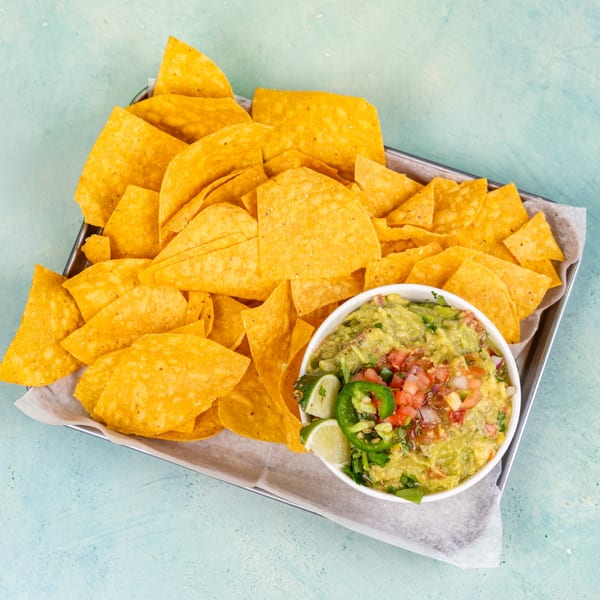 A metal tray filled with tortilla chips and a bowl of guacamole topped with pico de gallo.