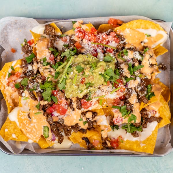 A tray of loaded nachos with ground beef, cheese sauce, pico de gallo, guacamole, and cilantro.