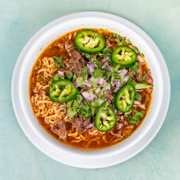 Top-down view of a ramen bowl with beef, cilantro, red onions, and jalapeño slices.