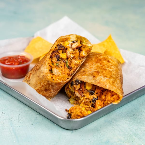 Two halves of a burrito filled with rice, beans, corn, and chicken, served with salsa and chips.