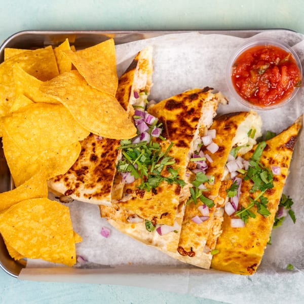 Golden-brown quesadilla slices topped with red onion and cilantro, served with tortilla chips and salsa.